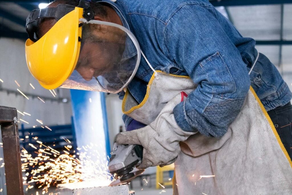 Worker using an angle grinder with full protective gear in a manufacturing facility