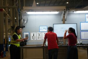 Workplace trainer explaining procedures to workers at an industrial workstation